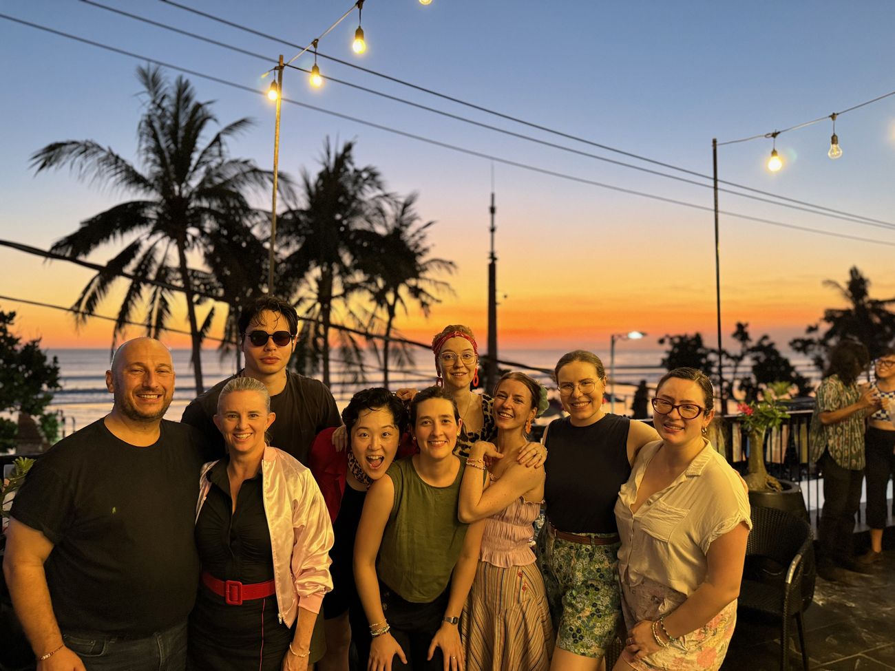 A group of dancers together at sunset under palm trees and string lights in Bali.